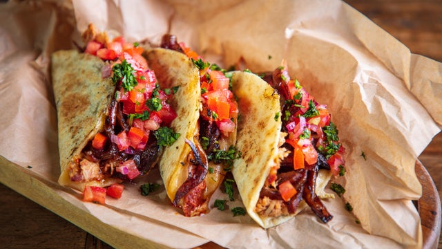 Serving of tacos with shredded roast pork and cheese filling on brown paper in wooden plate 